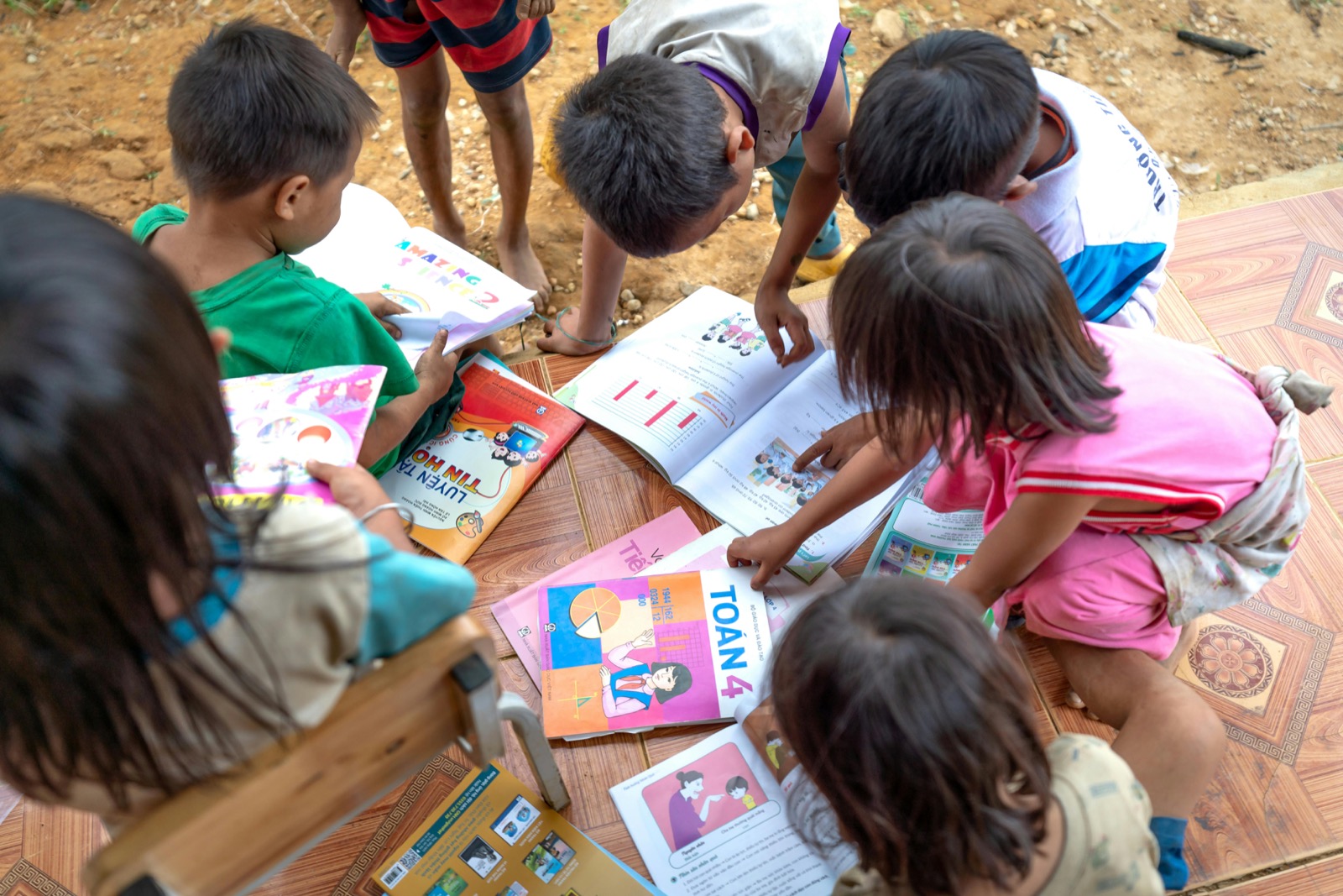 Children gathered around colorful learning books during a collaborative reading activity.